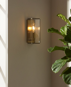 Wall-mounted light fixture on a neutral wall with a plant to the right