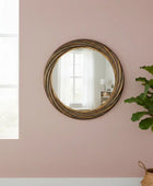 Round gold-framed mirror on a pink wall with a plant in the foreground