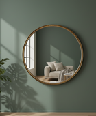 Round mirror on a green wall with a plant and chair reflection
