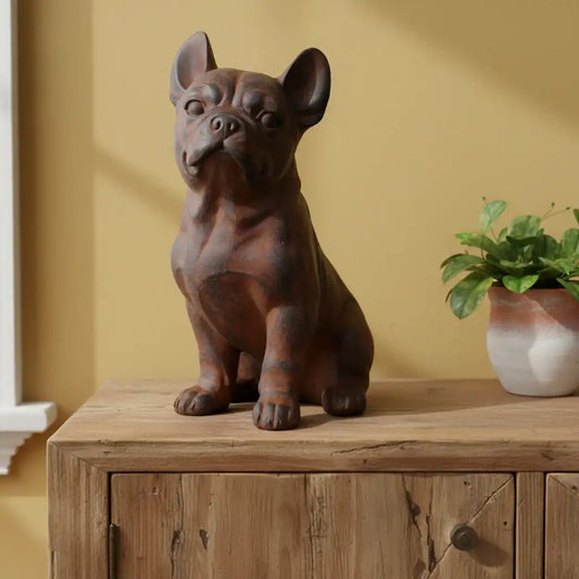 Decorative statue of a dog on a wooden surface with a plant in the background