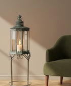 Decorative lantern with a candle on a stand next to a green armchair in a room.