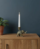 Decorative elephant candle holder with a candle on a wooden surface against a dark blue wall.