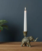 Bronze elephant candle holder with a lit white candle on a wooden surface against a dark blue wall.