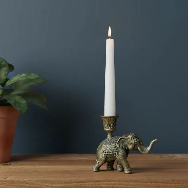 Bronze elephant candle holder with a lit white candle on a wooden surface against a dark blue wall.