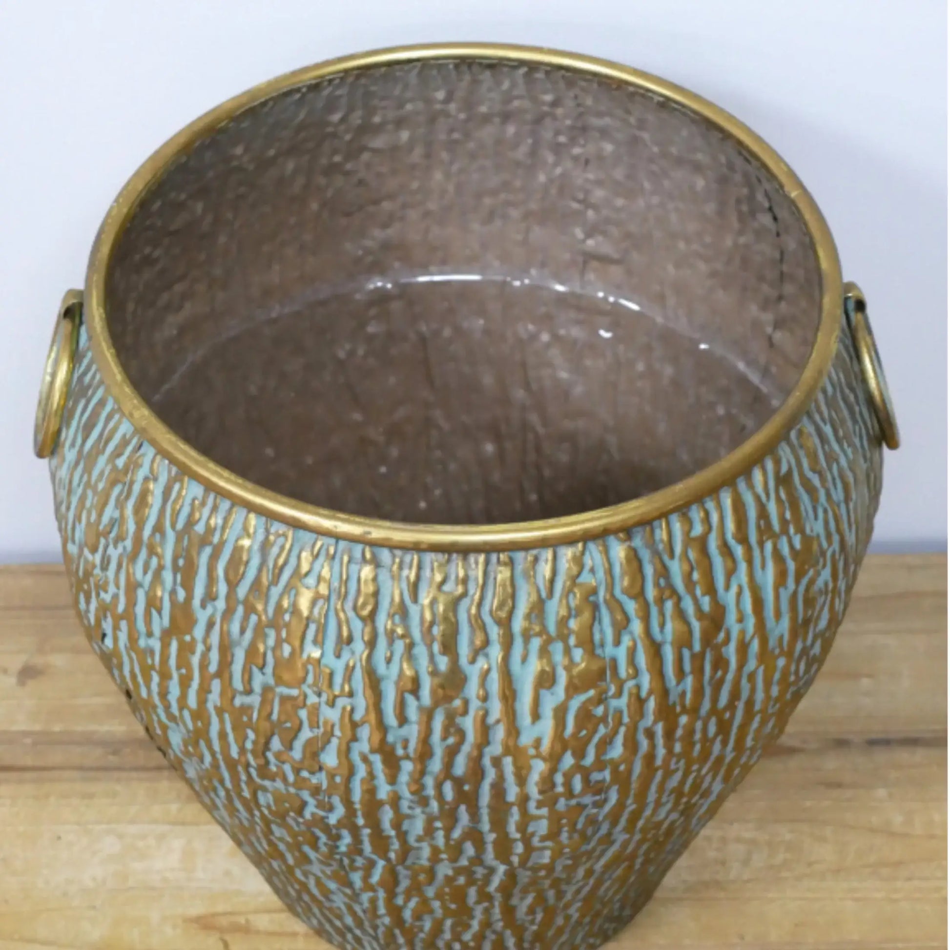 Decorative metal pot with textured surface and gold handles on a wooden surface.