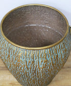 Decorative metal pot with textured surface and gold handles on a wooden surface.