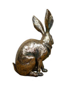 Bronze rabbit sculpture on a wooden surface with a gray background