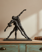 Bronze sculpture of two figures on a wooden surface with a plant and book in the background