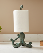 Decorative candle holder with a white candle on a surface next to a potted plant and book.