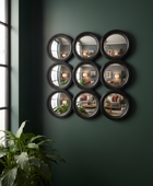 Nine circular mirrors arranged in a grid on a dark green wall with a plant to the left.