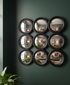 Nine circular mirrors arranged in a grid on a green wall with reflections of a living room.