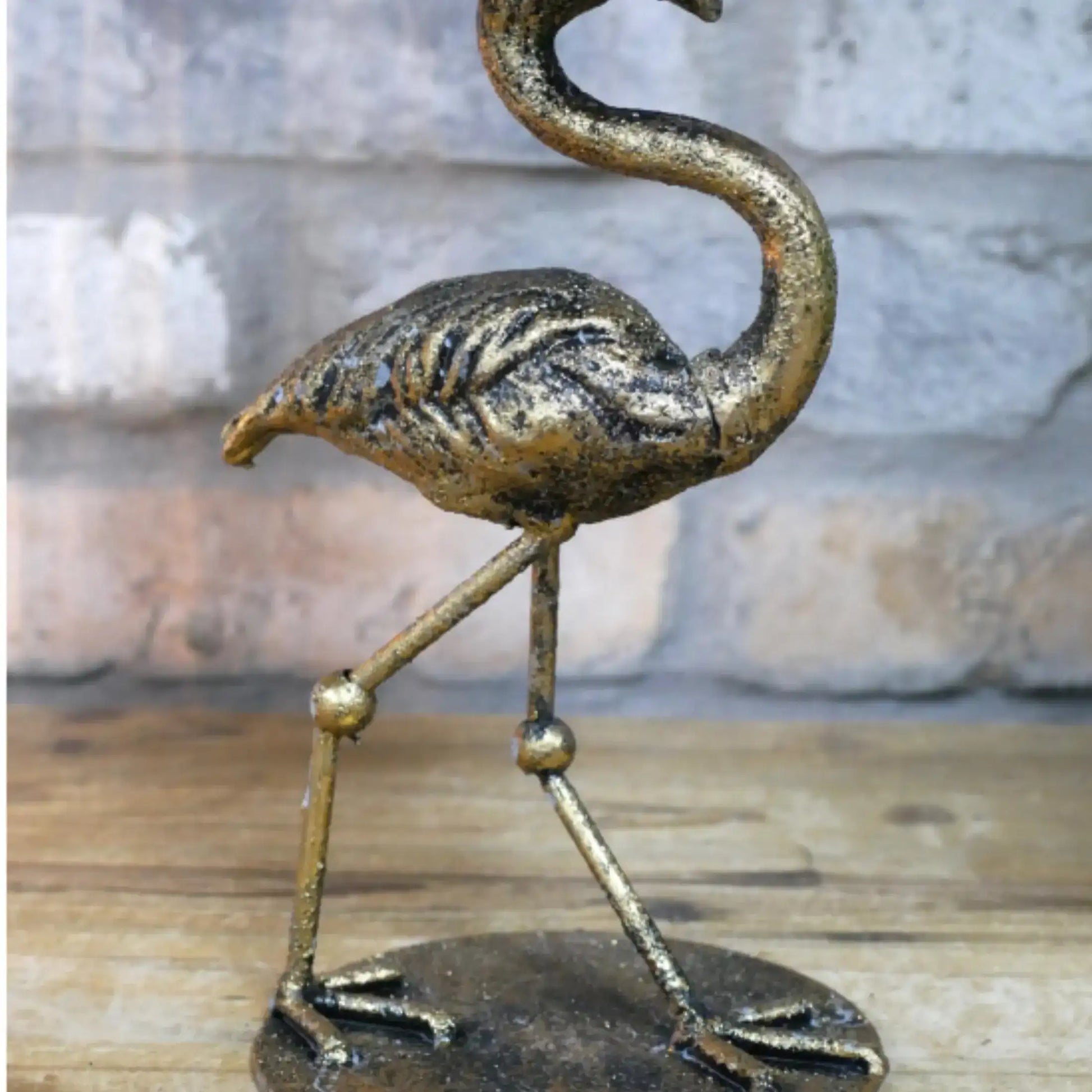 Bronze flamingo sculpture on a wooden surface with a stone wall background
