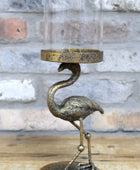 Decorative metal flamingo candle holder with a glass cover against a stone wall background.