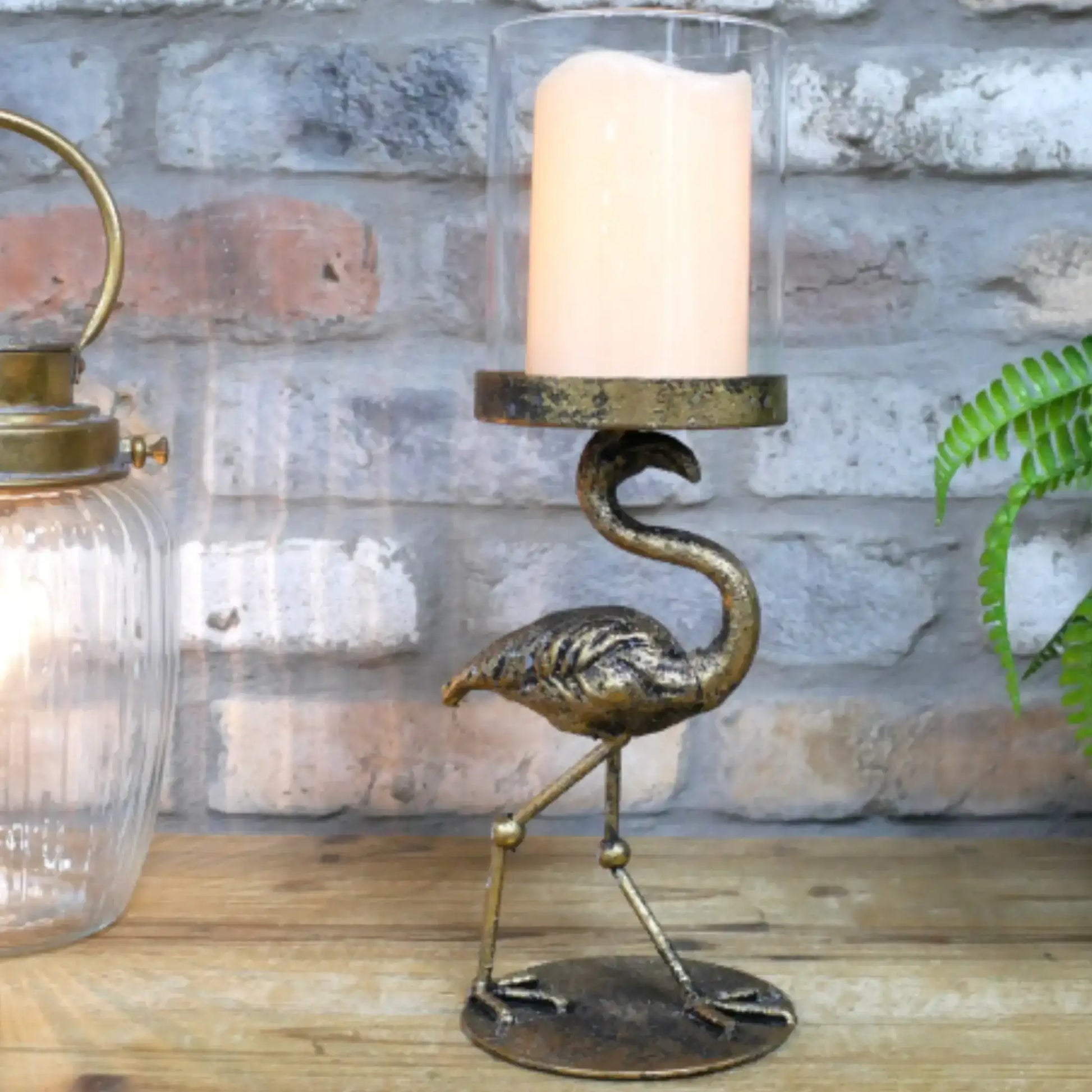 Bronze flamingo candle holder with a candle on a wooden surface against a stone wall.