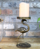Bronze flamingo candle holder with a candle on a wooden surface against a stone wall.