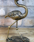 Bronze flamingo sculpture on a wooden surface with a stone wall background