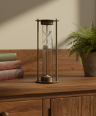 Hourglass on a wooden surface with books and a plant in the background