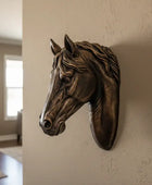 Bronze horse head sculpture on a wall in a room with a plant and window.