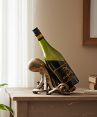 A green wine bottle with a black and gold label is propped up by a decorative octopus-shaped metal stand on a wooden table in a styled interior setting.