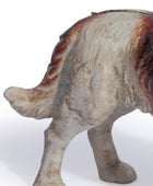 A close-up of a ceramic dog figurine showing its rear and side profile, featuring a textured off-white glaze with reddish-brown and black accents, set against a plain white background.