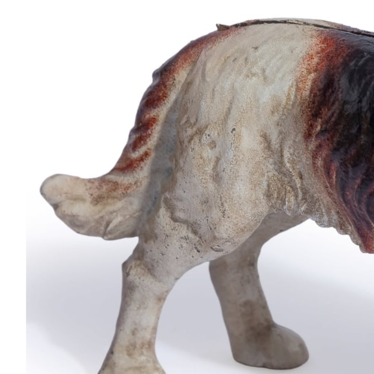 A close-up of a ceramic dog figurine showing its rear and side profile, featuring a textured off-white glaze with reddish-brown and black accents, set against a plain white background.