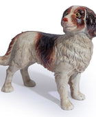 A vintage ceramic dog figurine, likely a spaniel or retriever, featuring a glossy glaze with cream, brown, and black coloring. The figurine is posed standing and photographed against a clean white background.