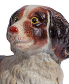 A ceramic dog figurine with a glossy brown and white glaze, featuring a white muzzle, dark brown ears, and yellow eyes, shown against a plain white background.