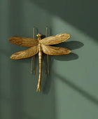 Gold dragonfly wall art against a light background with green leaves.