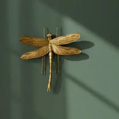 Gold dragonfly wall art against a light background with green leaves.
