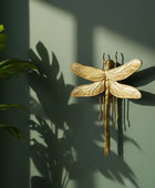 Gold dragonfly wall art on a green wall with a plant to the left.