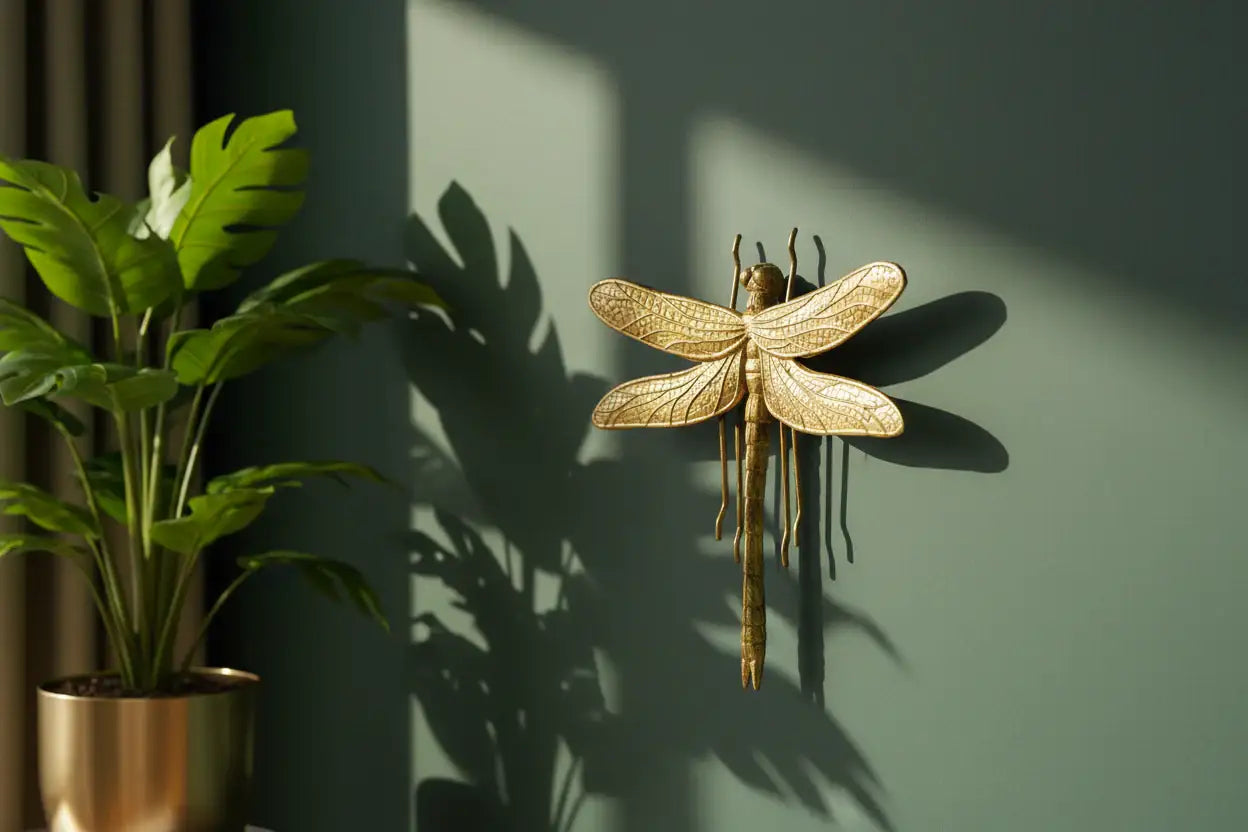Gold dragonfly wall art on a green wall with a plant to the left.