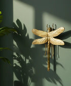 Gold dragonfly wall decoration on a green wall with plant shadows