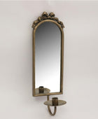 An antique-style wall sconce featuring an arched mirror with an ornate bronze frame and a matching candle holder below, mounted against a plain light gray wall.