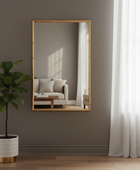 Gold-framed mirror on a wall with a plant and sofa in the reflection