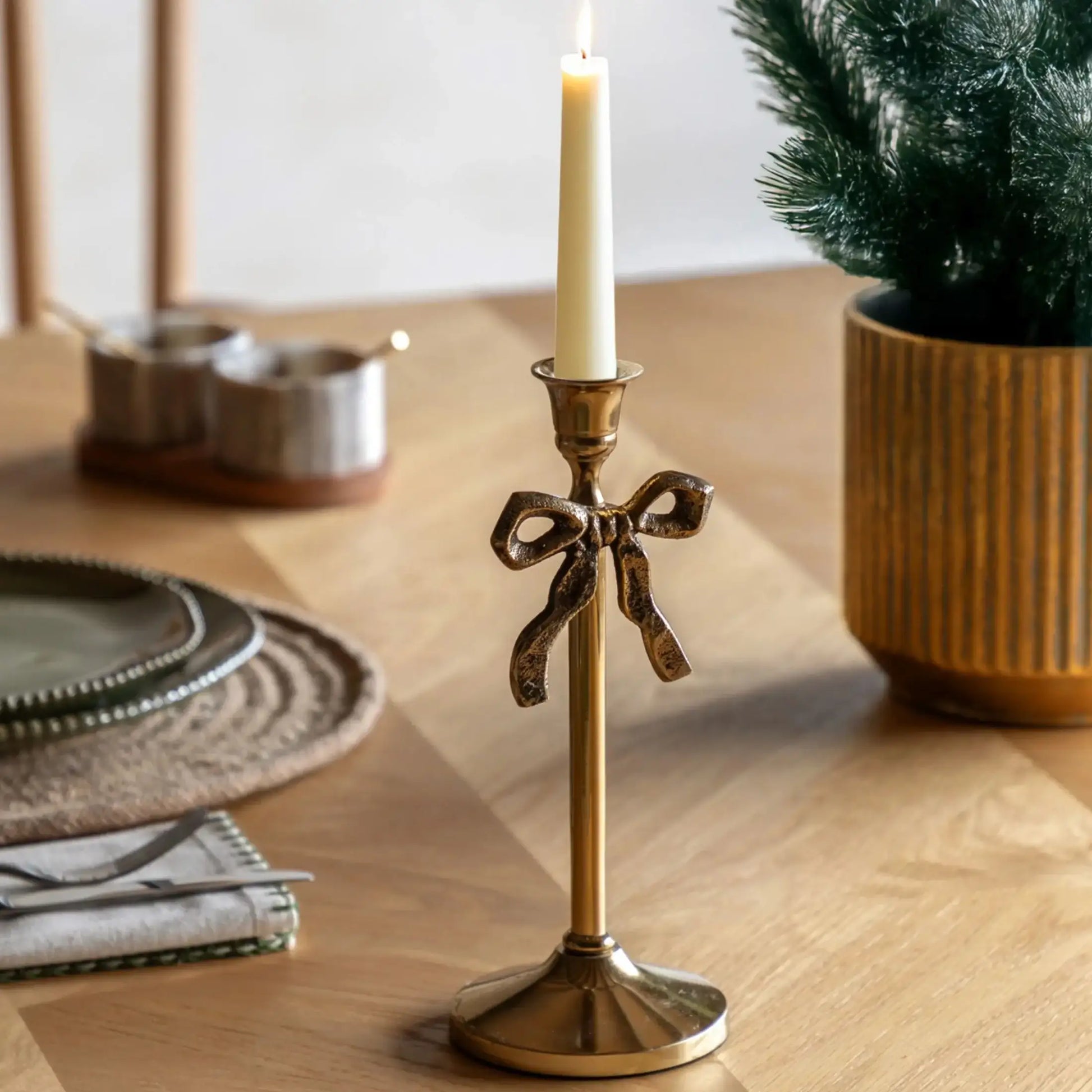 Gold candle holder with a bow design on a wooden table with a candle and decorative items.
