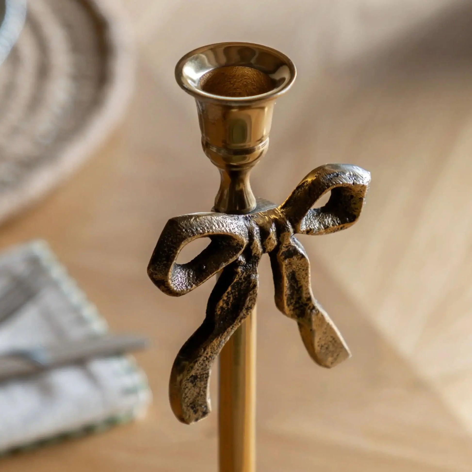 Bronze candle holder with bow design on a neutral background