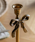 Bronze candle holder with bow design on a neutral background