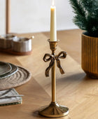 Gold candle holder with a bow design on a wooden table with a candle and decorative items.