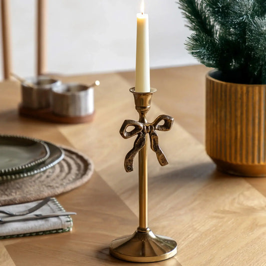 Gold candle holder with a bow design on a wooden table with a candle and decorative items.