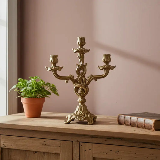 Decorative gold candelabra on a wooden surface with a plant and book in the background.