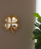 Decorative four-leaf clover mirror on a wall with a plant in the corner