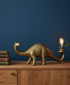 Gold dinosaur lamp with a light bulb on a wooden surface against a blue wall