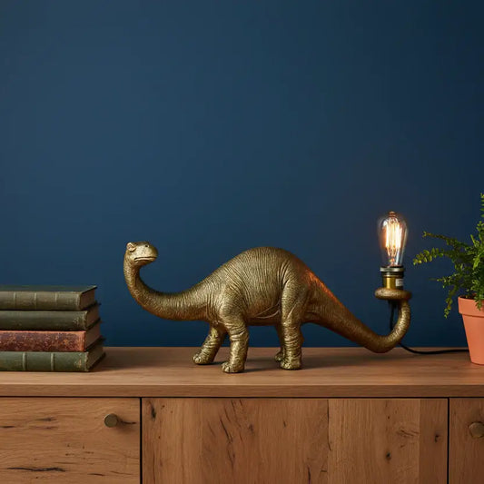 Gold dinosaur lamp with a light bulb on a wooden surface against a blue wall