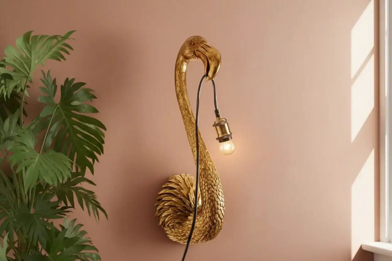 Gold flamingo-shaped wall lamp on a pink wall with a plant to the left.