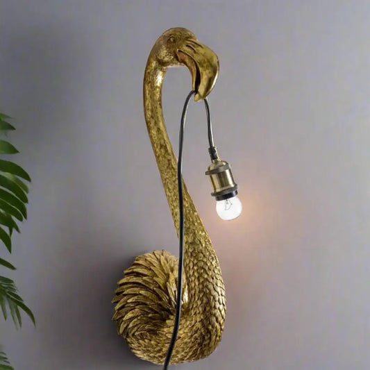 Gold flamingo-shaped wall lamp with a light bulb on a plain background