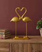 Gold flamingo sculpture on a wooden surface with a plant and books in the background.