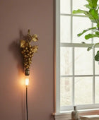 Decorative wall light with grape design next to a window with a plant