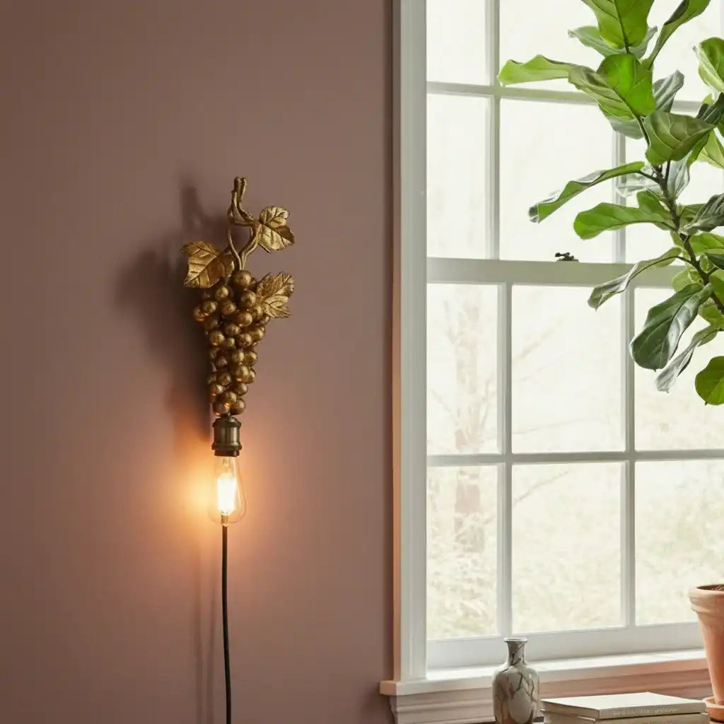 Decorative wall light with grape design next to a window with a plant