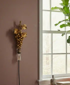 Decorative wall sconce with grape design on a wall next to a window with a plant.