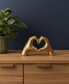 Gold hands forming a heart shape on a wooden surface with a plant in the background